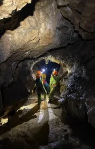 4 personnes en tenue de speleologie dans une galerie de la grotte de la Resurrection regardent le guide de speleologie 192x300
