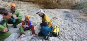 Trois personnes ecoutent un guide de speleologie a lentree du Puits des Bans dans le Devoluy 1536x728 1 300x142