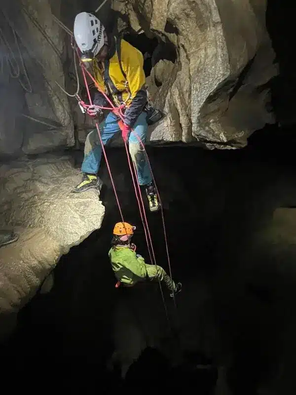 Un guide de speleologie assis en haut dun puits assure une personne qui descend en rappel dans une grotte