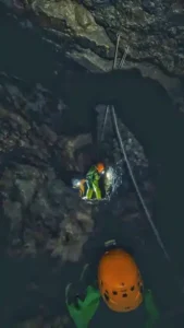 Un speleologue eclaire devant lui une personne qui descend en rappel dans le Puits des Bans 169x300