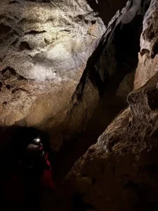 Une personne equipee dun casque et dune lampe frontale eclaire la galerie de la grotte de Orpierre 225x300