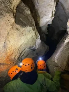 trois personnes equipes de casques et de lampes frontales observent lentree de la grotte de la Resurrection 225x300