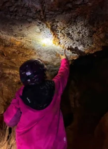 un enfant equipe dune veste rose et dun casque noir eclaire des stalactites dans une grotte a Sisteron 218x300