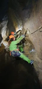 une personne equipe dun casque dun baudrier progresse sur une main courante dans une grotte des gorges dAgnielles 727x1536 1 142x300